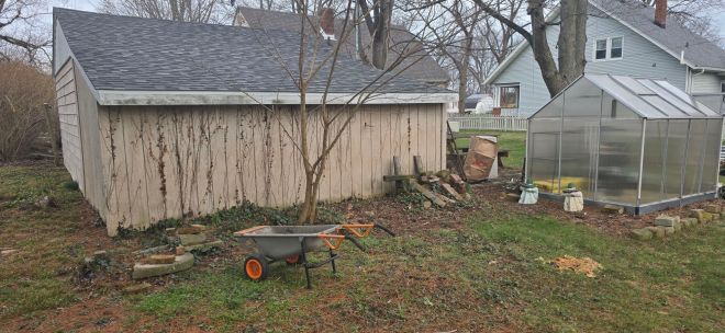 Behind the garage is overgrown and riddled with various types of paving stones and bricks.
